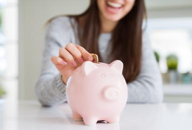 Young woman smiling putting a coin inside a piggy bank as savings for investment